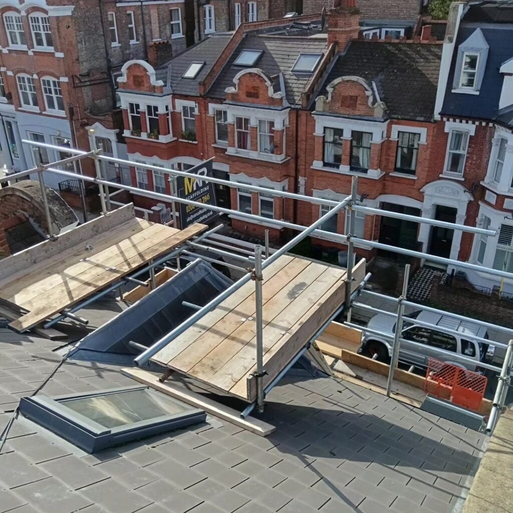 Roof scaffolding with guardrails above a row of Victorian terraced houses