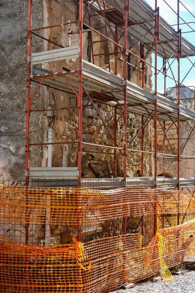 Scaffolding against a historic stone wall with safety netting at ground level